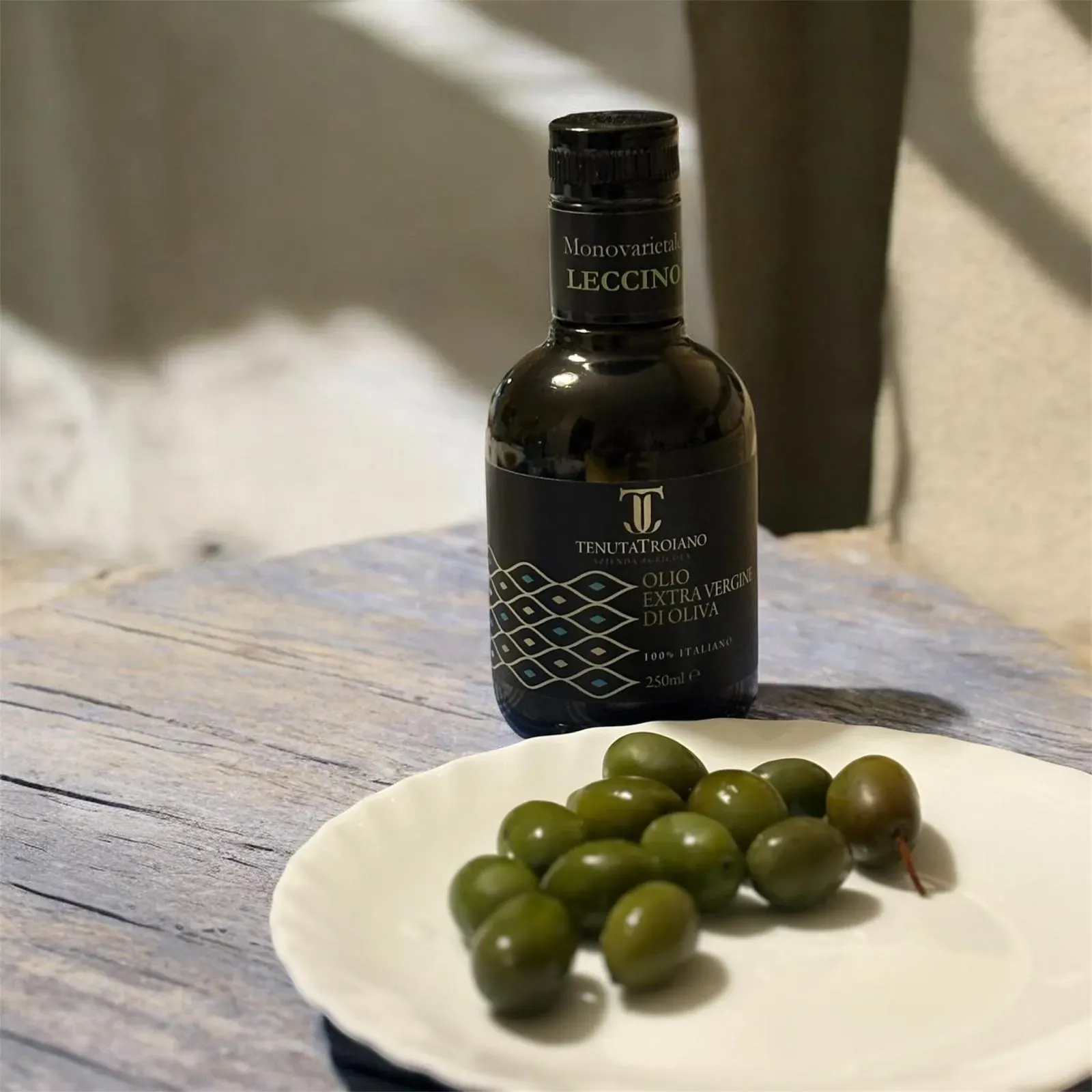 Bottiglia da 250 ml Tenuta Troiano accanto a un piatto di olive verdi.