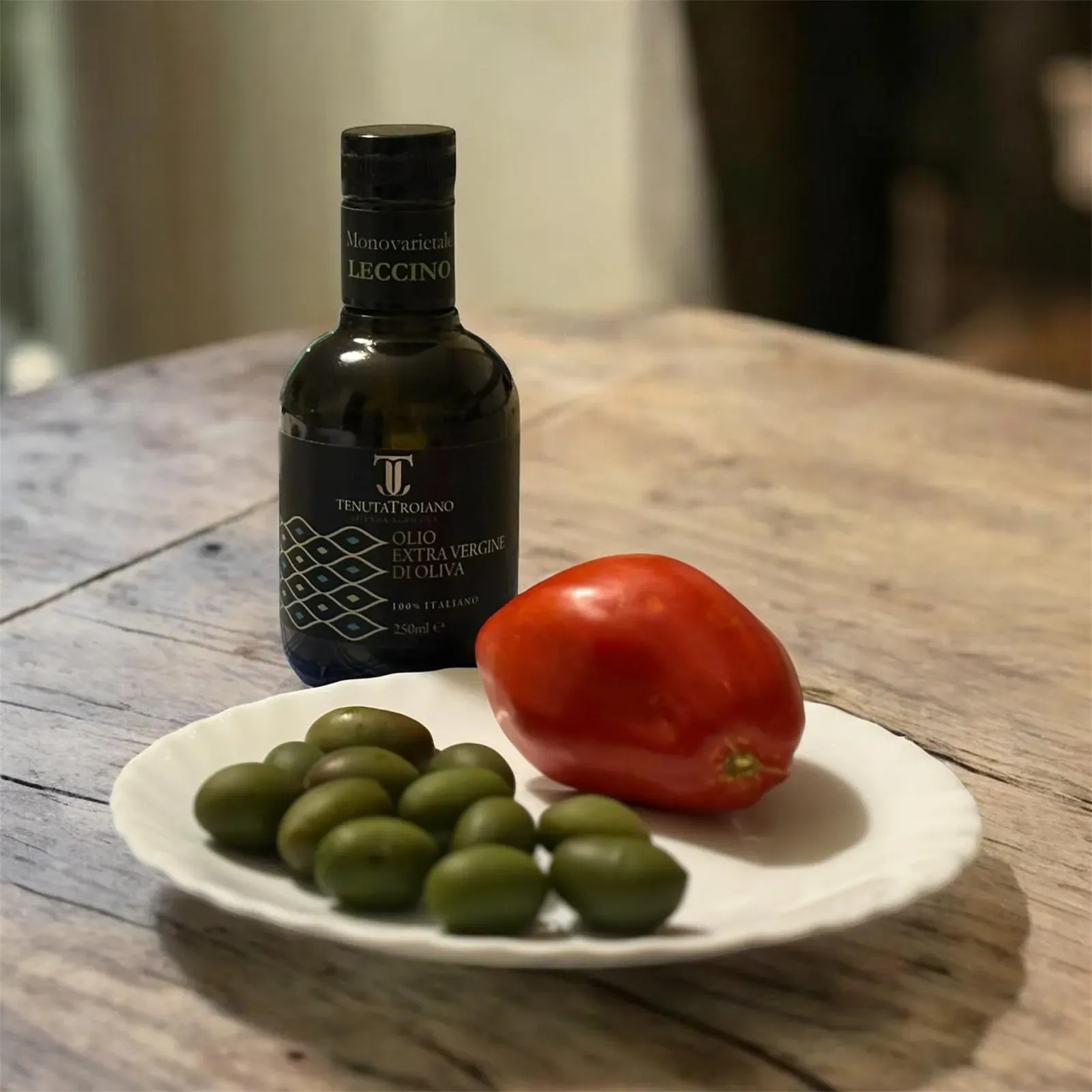 Bottiglia da 250 ml Tenuta Troiano dietro a un piatto di olive e pomodoro.