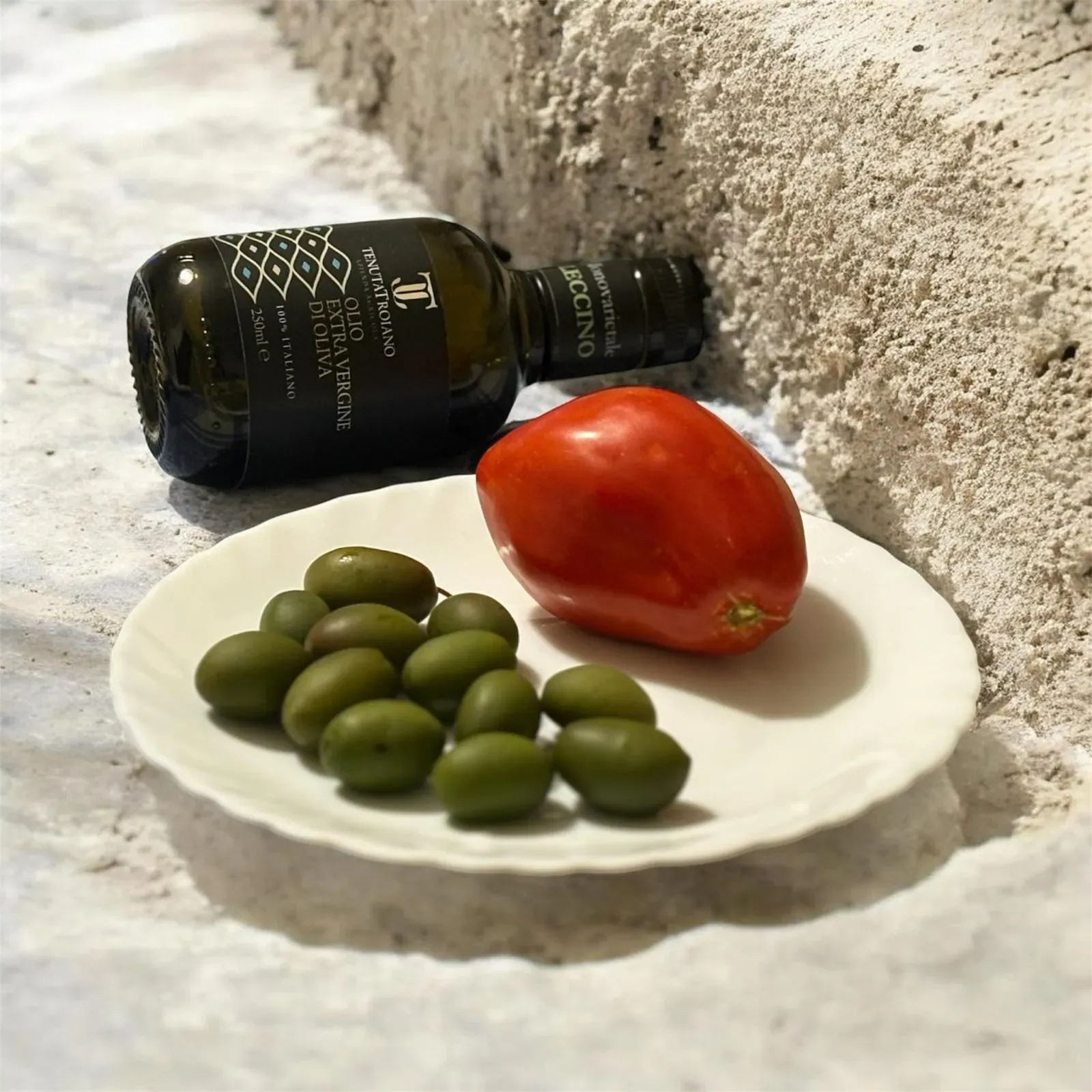 Bottiglia da 250 ml Tenuta Troiano distesa accanto a olive verdi e pomodoro.