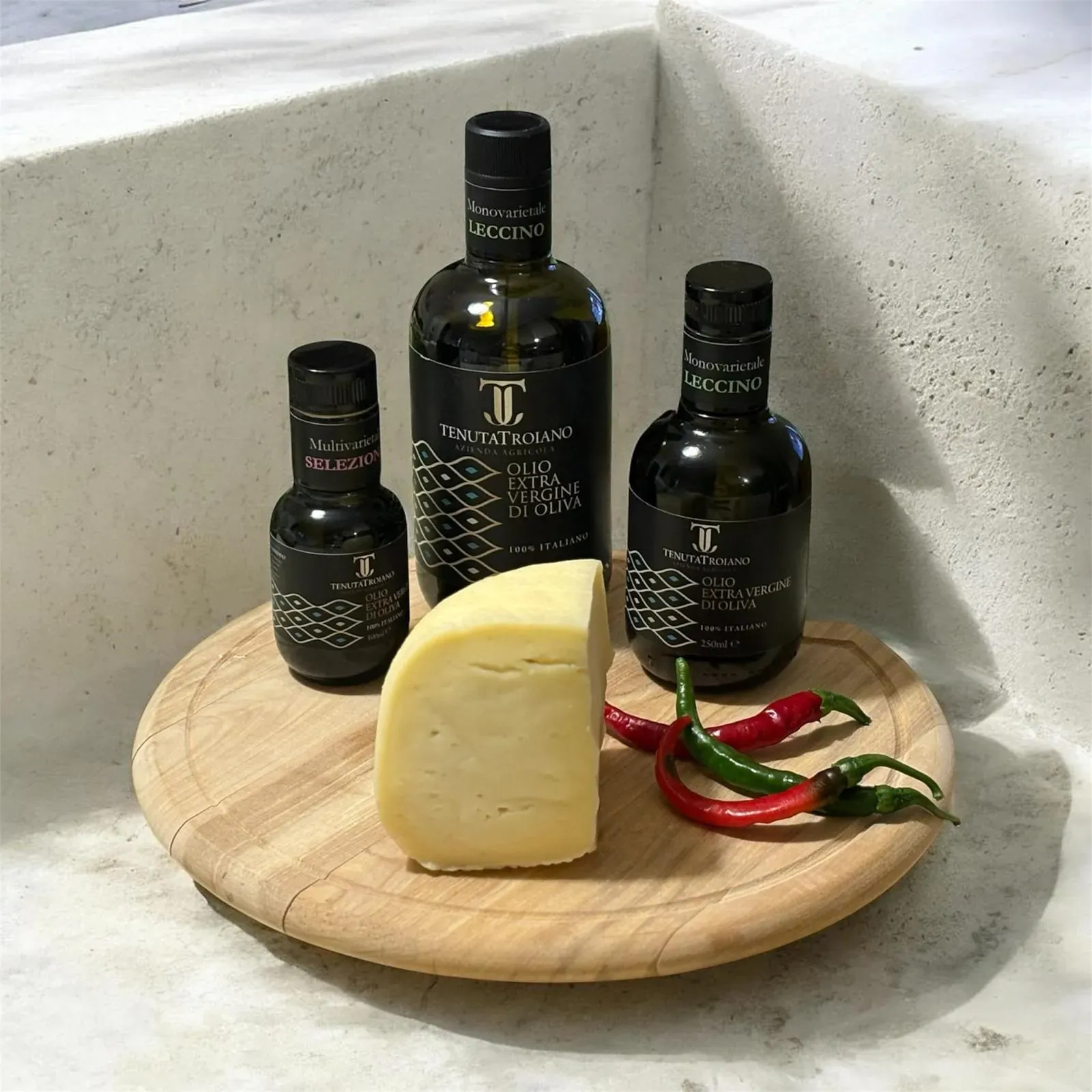Bottiglia da 500 ml Tenuta Troiano con altre bottiglie, formaggio e peperoncini su un tagliere.