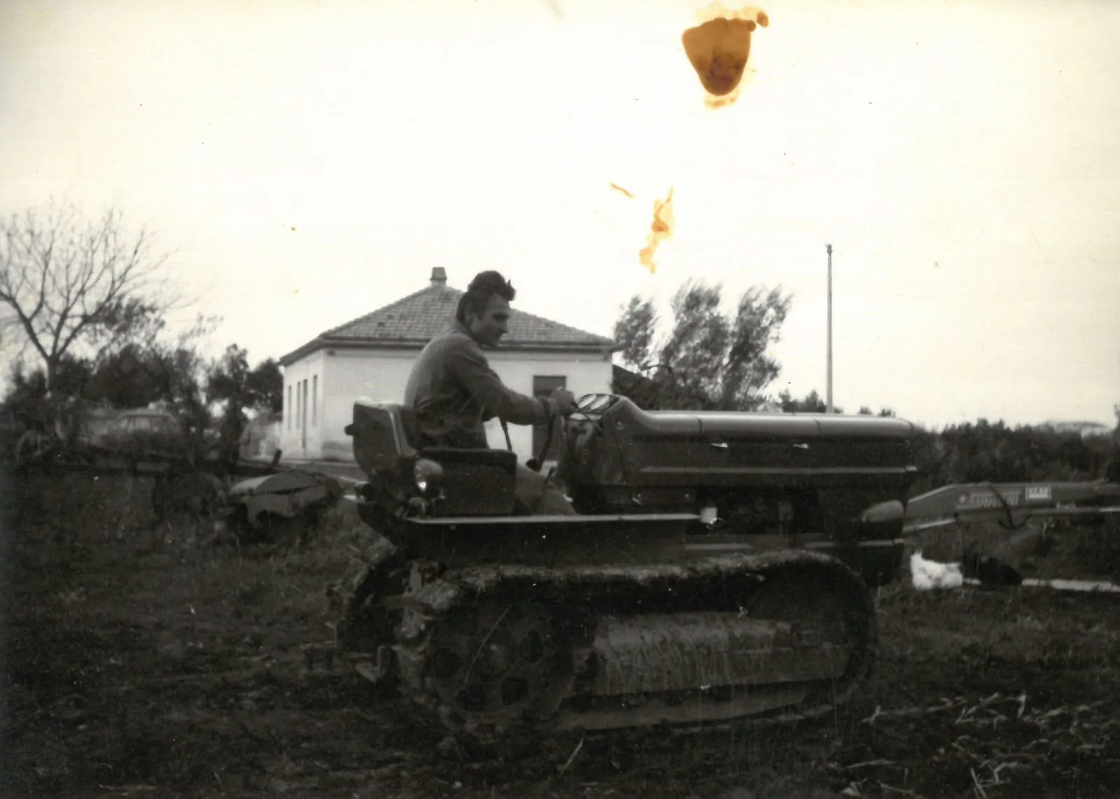 Una foto d’epoca: un uomo alla guida di un trattore cingolato, davanti a una casa di campagna.